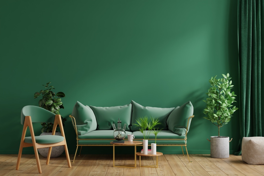 Uma sala de estar com as paredes e a decoração em um tom verde mais escuro, com plantas, um sofá, uma cadeira ao lado e uma mesa pequena no centro.
