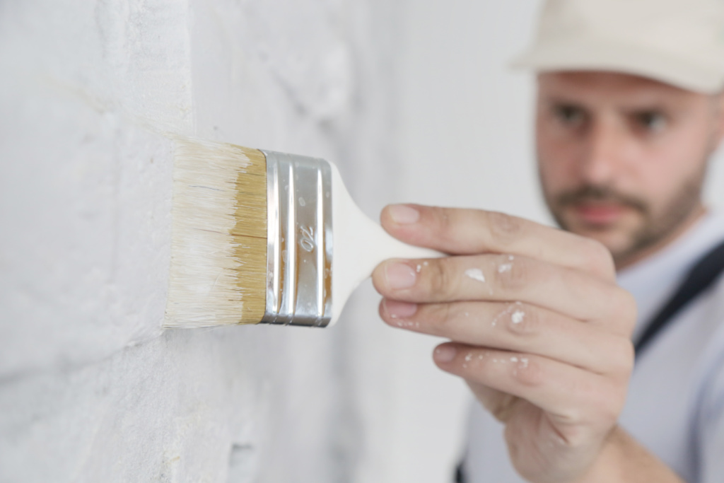 Homem com pincel passando tinta na parede.