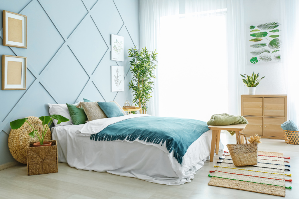 Decoração de um quarto com a cor azul e plantas pelo quarto, uma cama de casal com almofadas e uma manta decorativa no tom azul mais escuro, e um móvel em tom madeira que orna muito bem no ambiente.